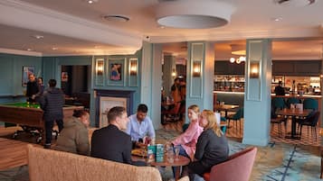 A hotel lobby with a pool table, bar area, and seating for guests.