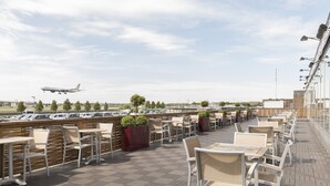 Terraza en la azotea con mobiliario exterior, vista a un aeropuerto y coches estacionados al fondo.
