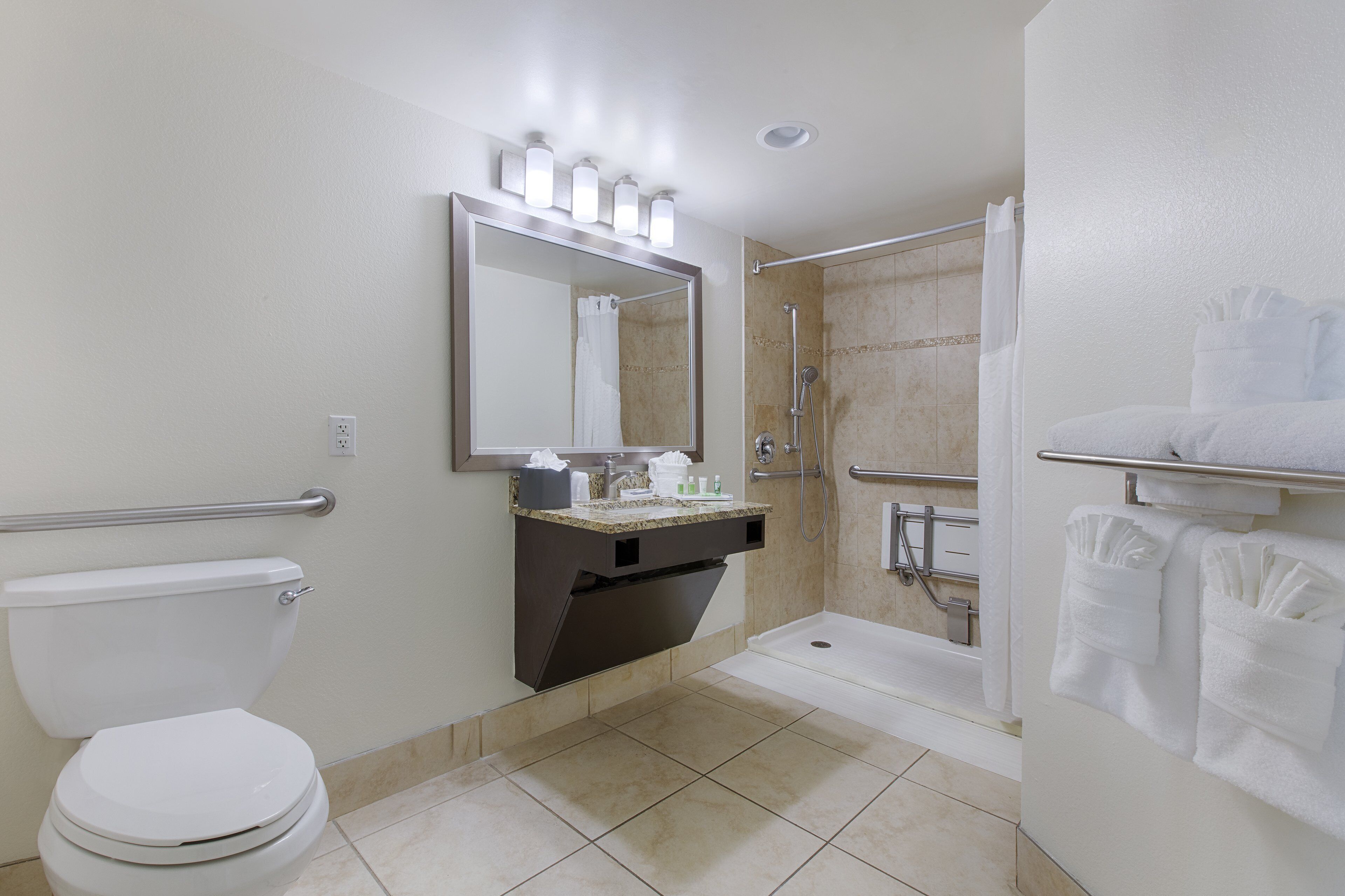 Un baño moderno con inodoro, lavamanos, espejo, ducha y toallero.