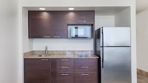 A kitchen with dark wood cabinets, a stainless steel refrigerator, and a granite countertop. - Holiday Inn Resort Daytona Beach Oceanfront by IHG (Daytona Beach)