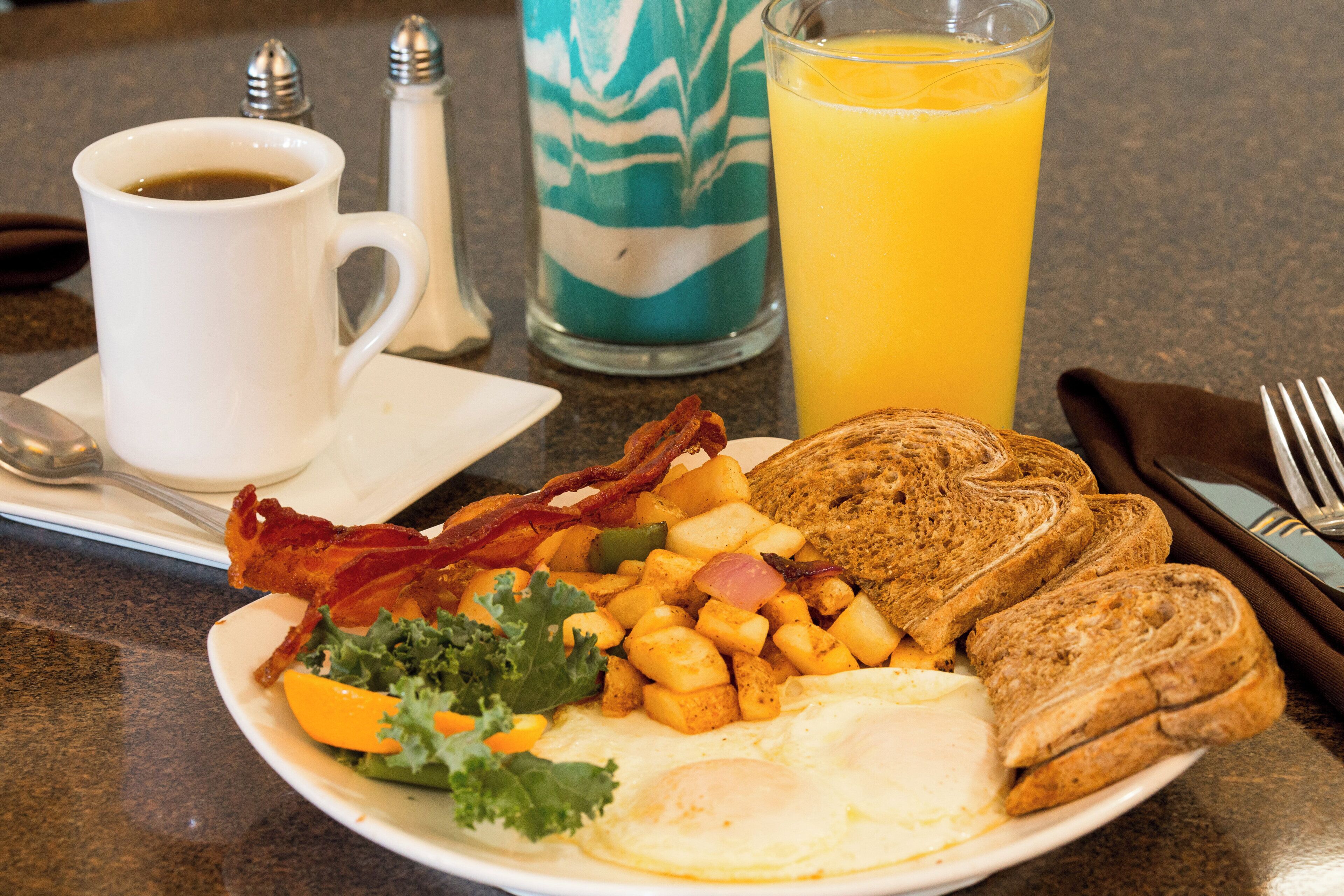 A breakfast plate with eggs, bacon, toast, potatoes, and a glass of orange juice.