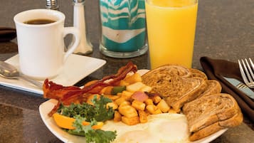 A breakfast plate with eggs, bacon, toast, potatoes, and a glass of orange juice.