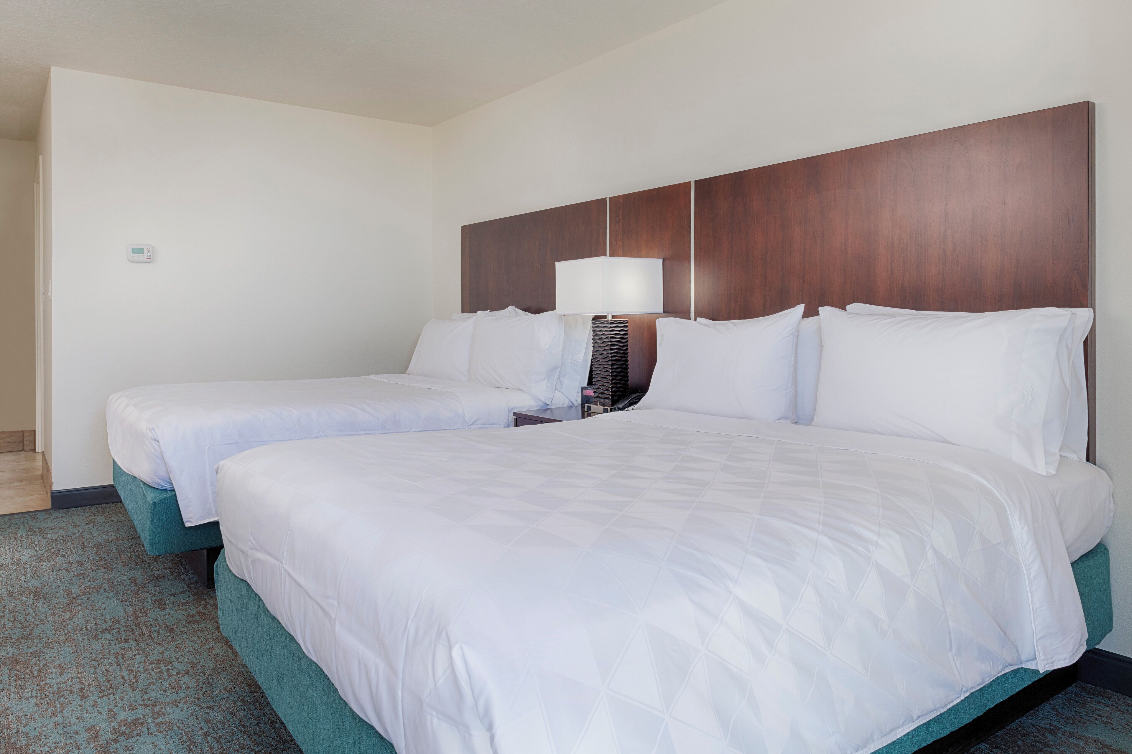 Une chambre d’hôtel avec deux lits, une table de chevet et un thermostat fixé au mur.