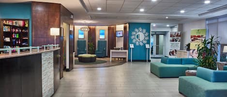A hotel lobby with a reception desk, seating area, and a wall with a decorative mirror.