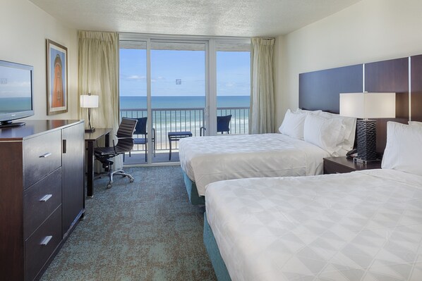 A hotel room with two beds, a desk with a chair, a television, and a view of the ocean through large windows. - Holiday Inn Resort Daytona Beach Oceanfront by IHG (Daytona Beach)