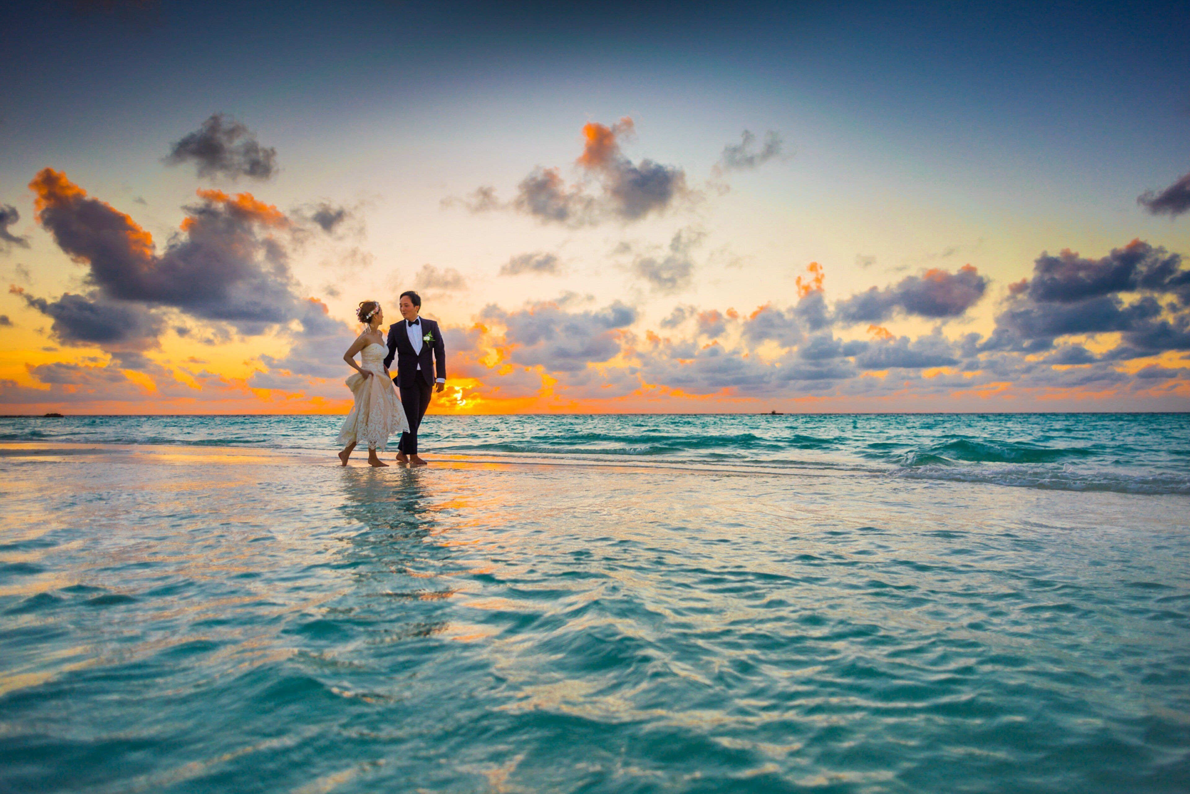 A couple standing on a beach with a sunset in the background.