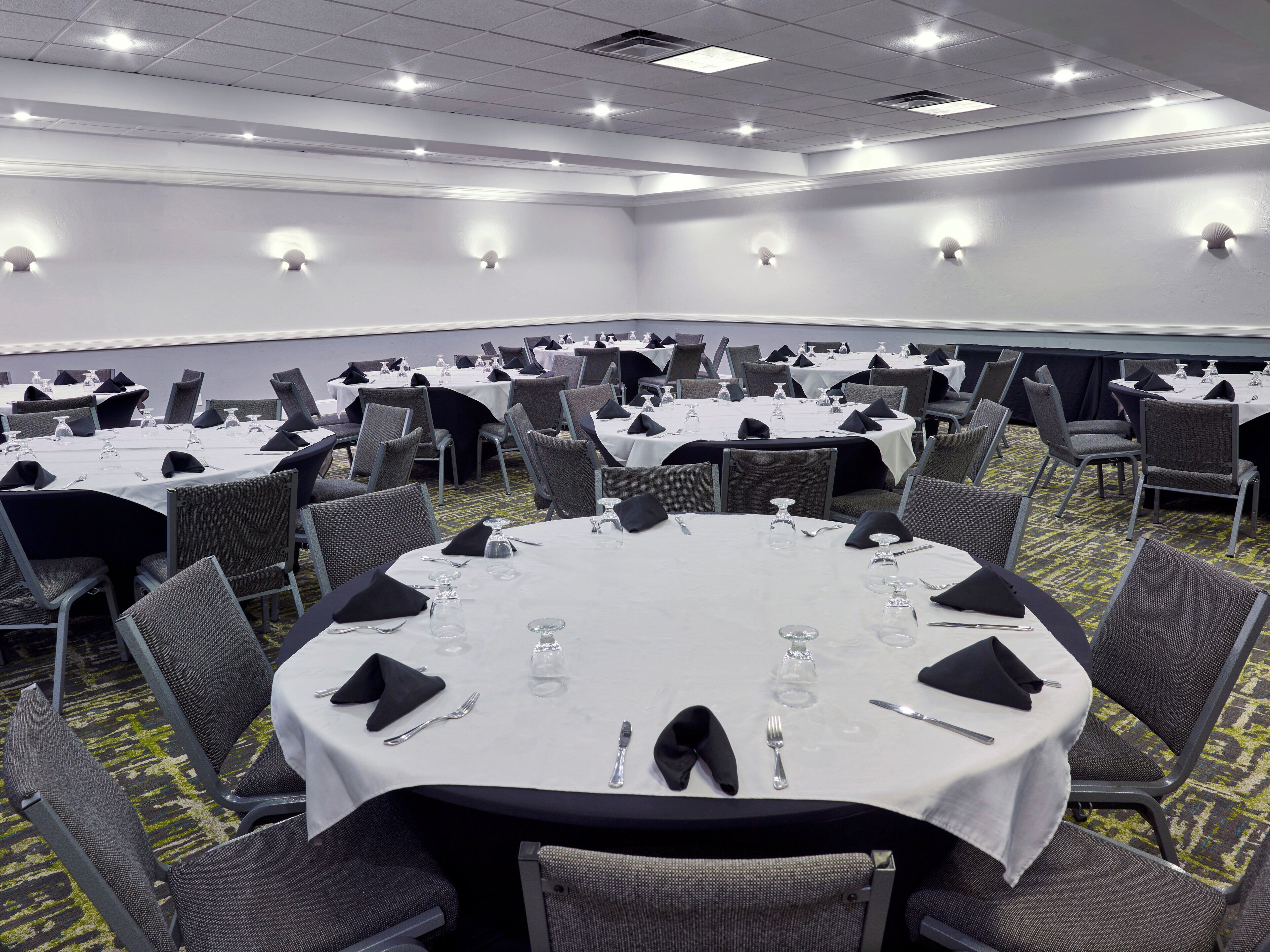Une salle de conférence dotée de plusieurs tables rondes, chacune étant agrémentée de chaises et de couverts.