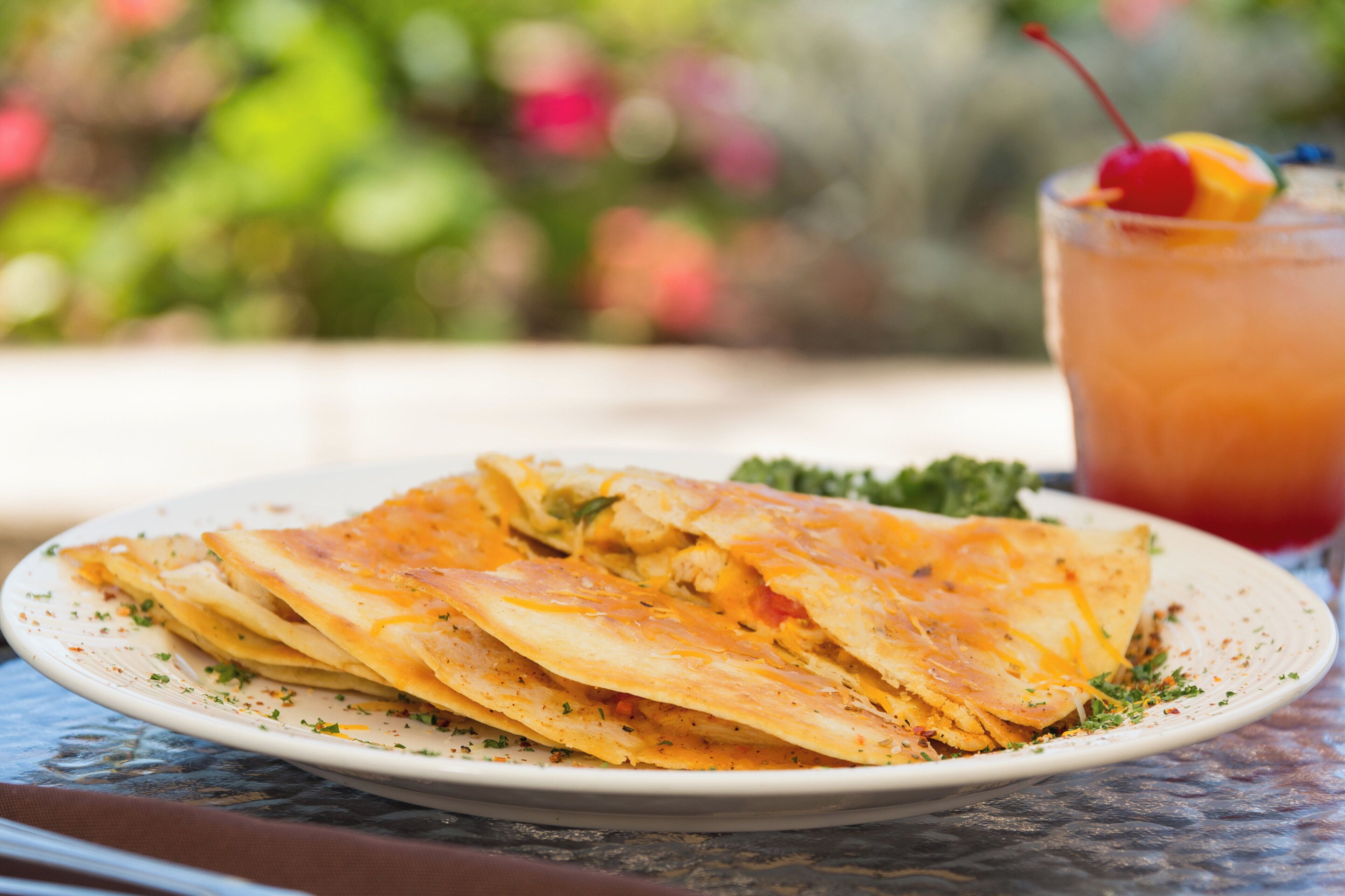 A plate of quesadillas with a side of sauce and a drink with a cherry on the rim.