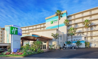 Edificio del Holiday Inn Resort con un cartel llamativo, un bar y restaurante cubierto frente al océano, y un área de estacionamiento con un camión.