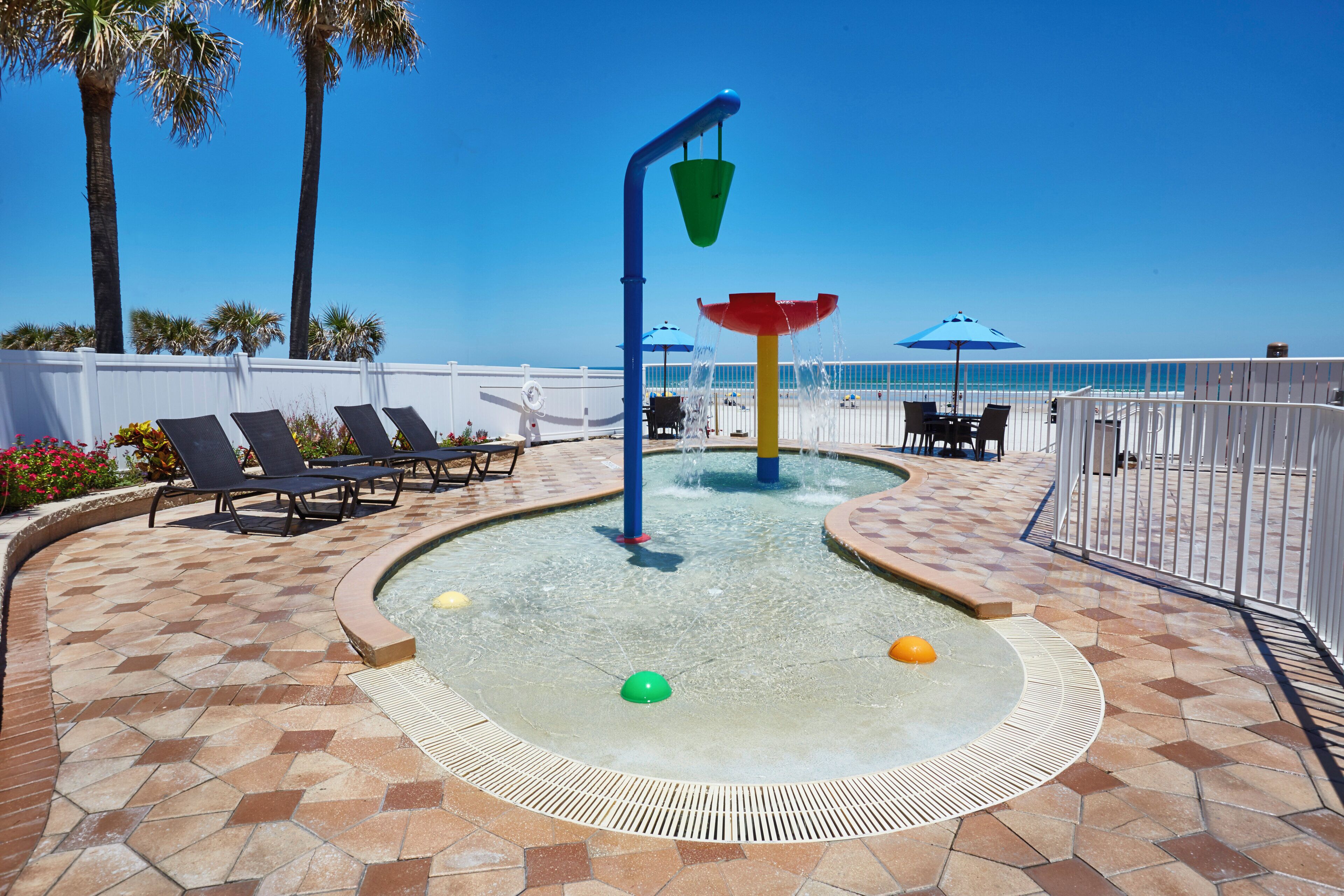 A pool area with a water feature, lounge chairs, and a view of the ocean.