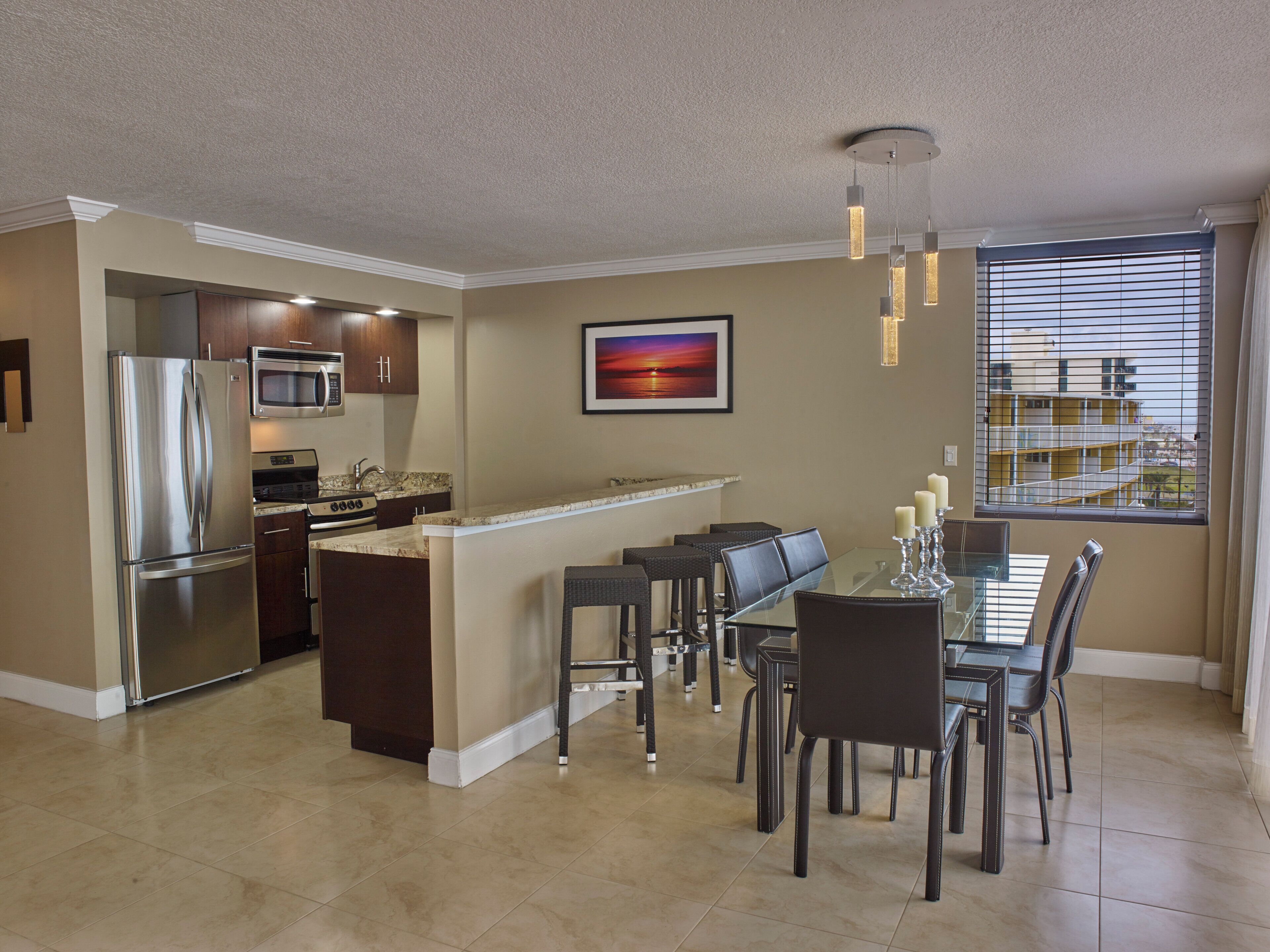 A modern kitchen with a built-in refrigerator, microwave, and oven. There is a dining area with a glass table and chairs.