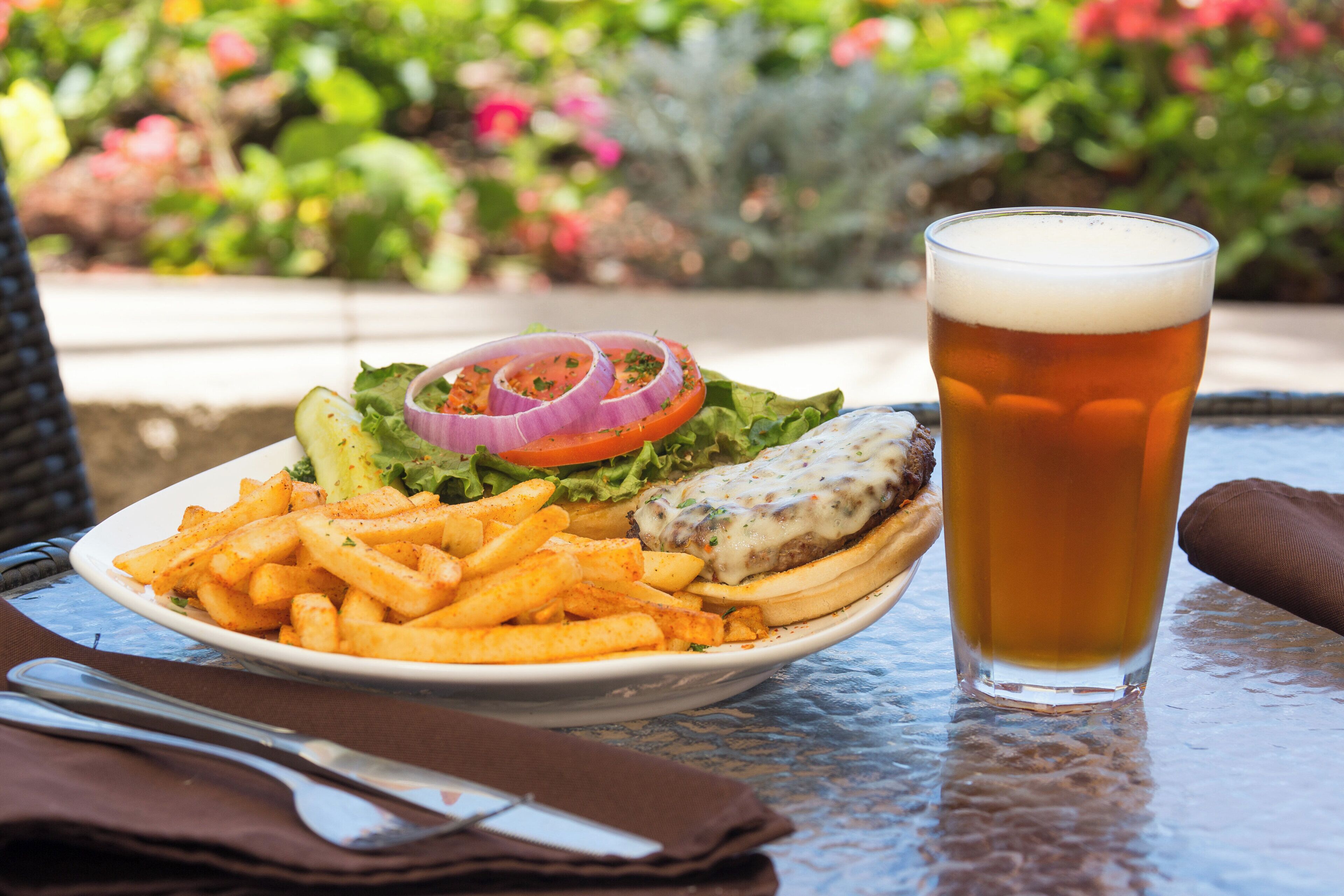 Una comida con una hamburguesa, papas fritas y una cerveza en una mesa al aire libre.