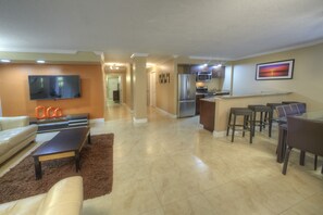 A modern living room with a sofa, coffee table, and a TV mounted on the wall. There is a kitchen area with a refrigerator and microwave. - Holiday Inn Resort Daytona Beach Oceanfront by IHG (Daytona Beach)