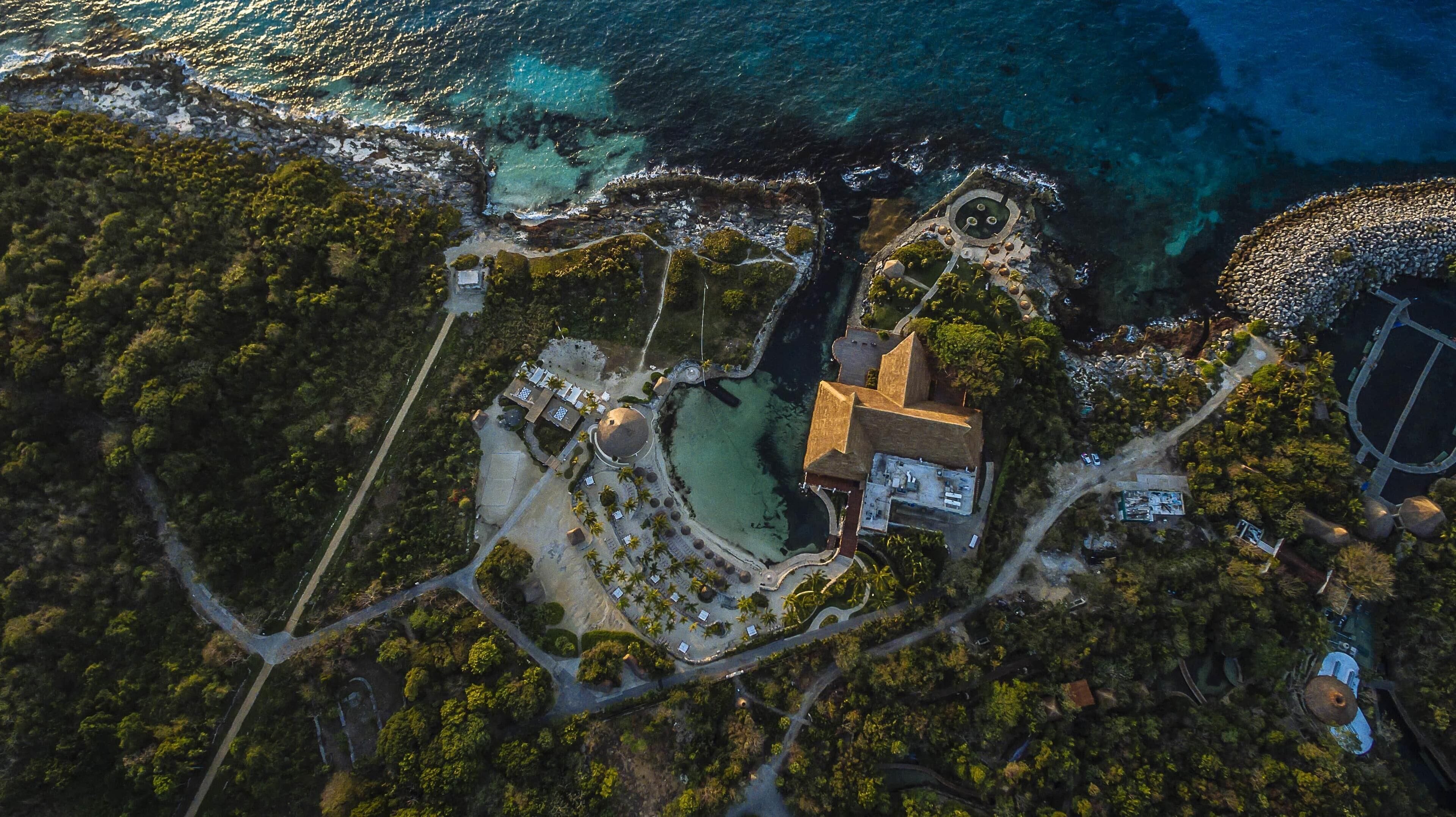 An aerial view of a coastal property with a central building, a large sandy area, and a rocky shoreline.