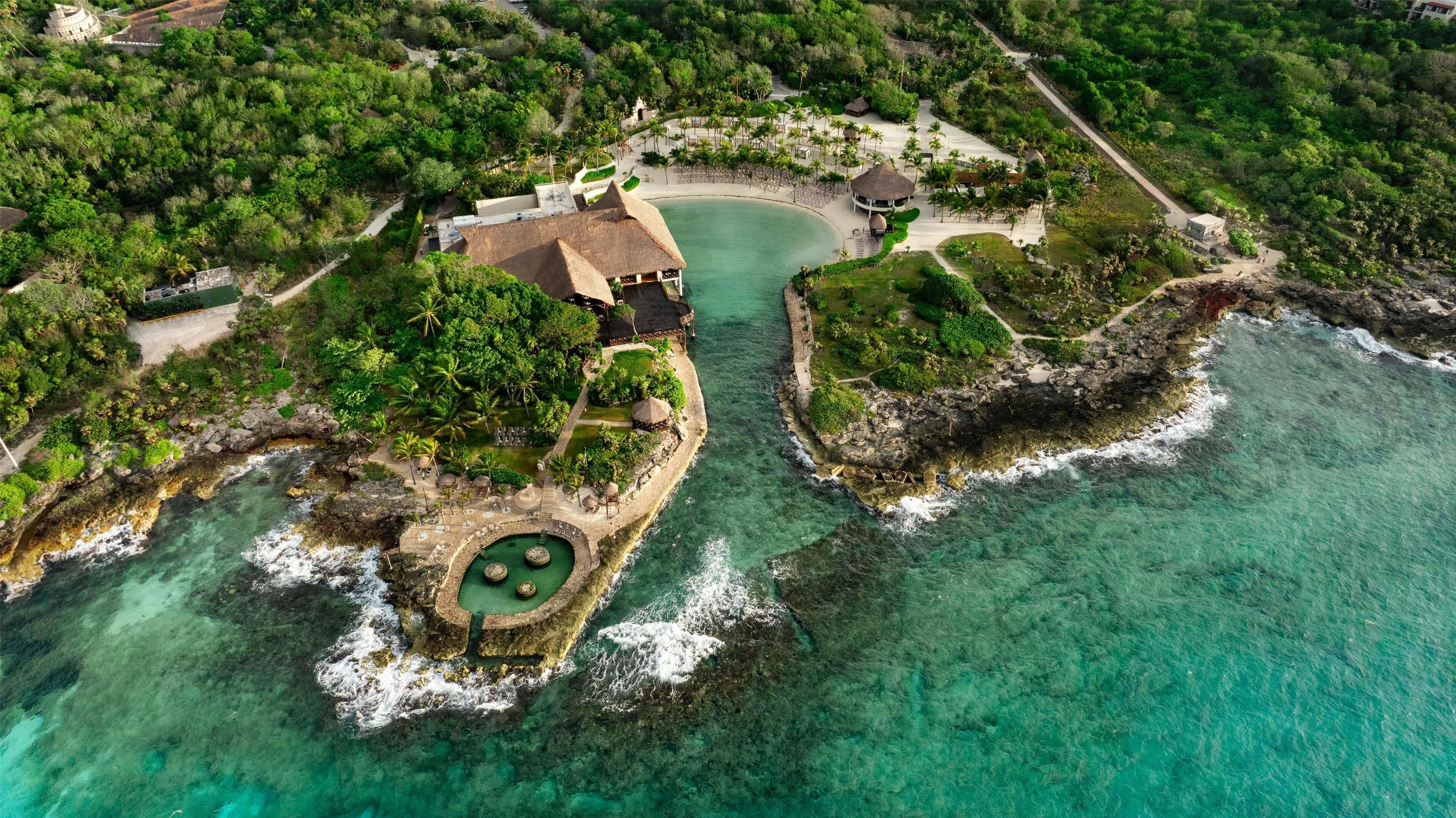 Vue aérienne d’un complexe hôtelier doté d’une piscine circulaire centrale, entourée d’une végétation luxuriante et d’une zone de plage.