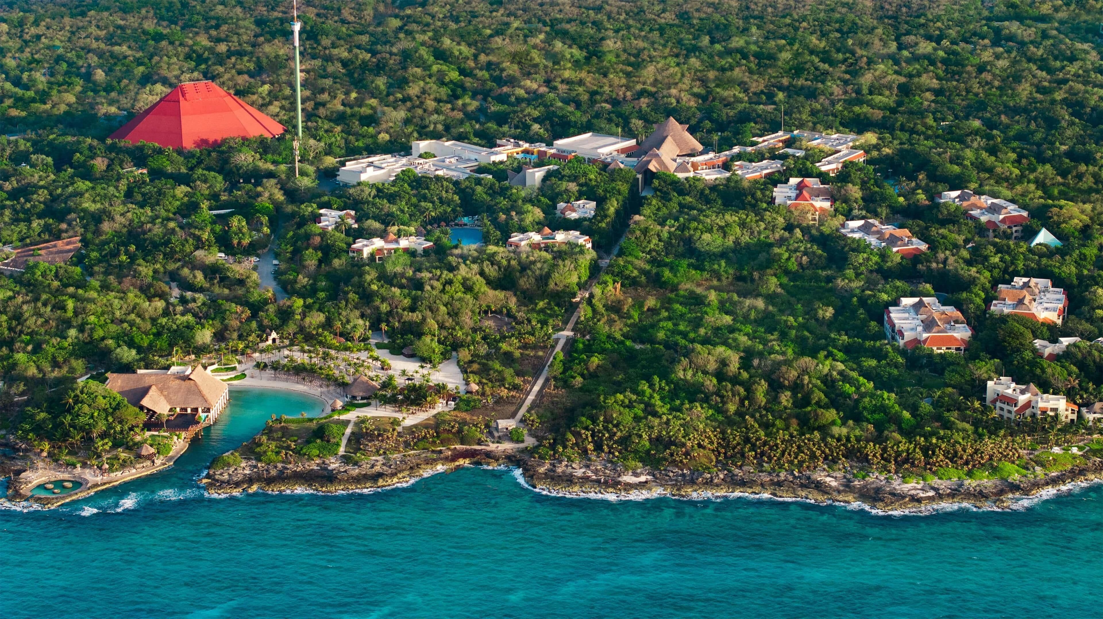 An aerial view of a resort with multiple buildings, a central red-roofed structure, and a beachfront area with a pool.
