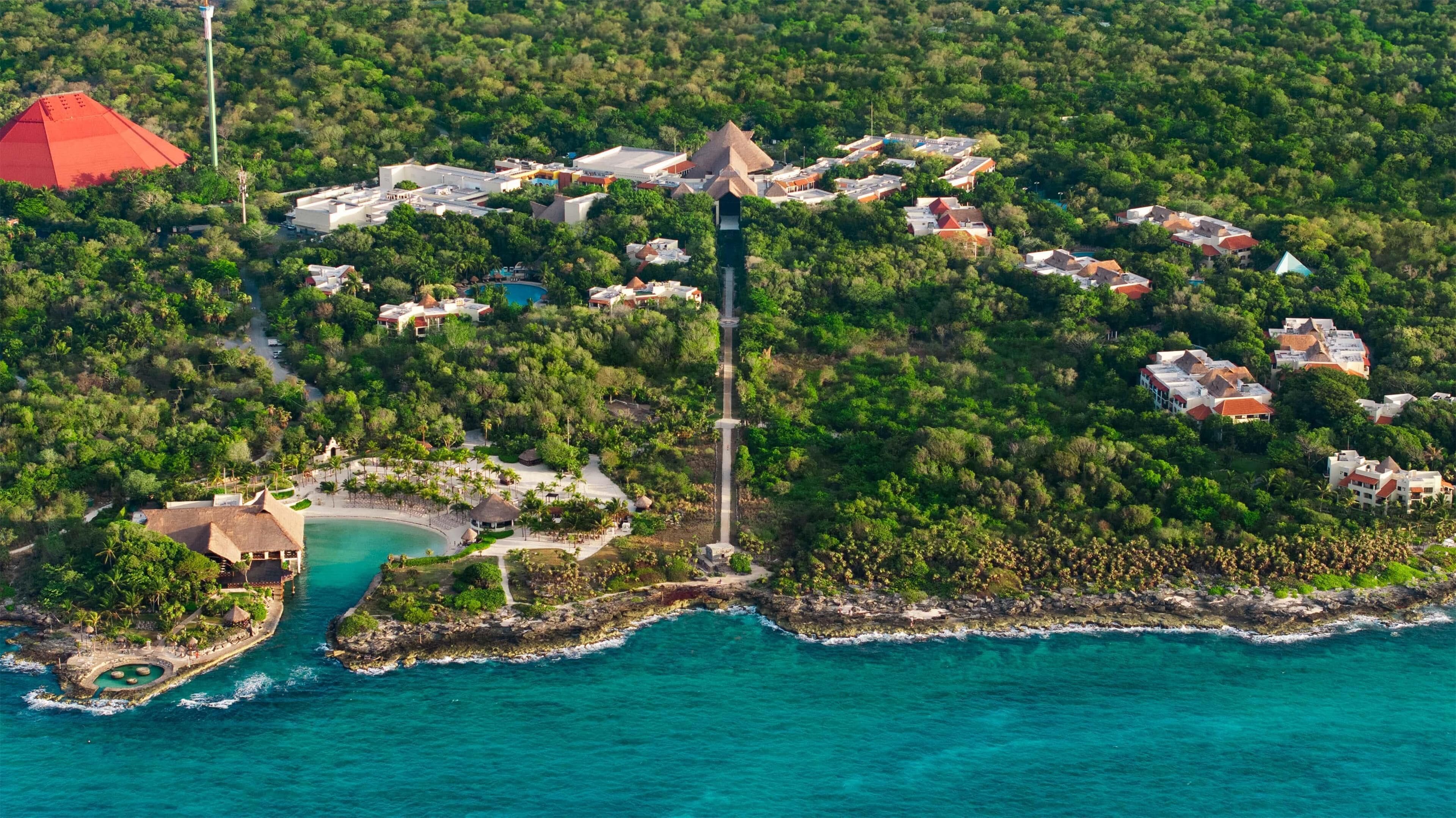 Vista aerea di un resort costiero con una torre centrale, diversi edifici e una spiaggia.