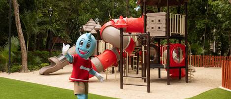 A mascot in a playground with a slide, climbing structures, and a gazebo.