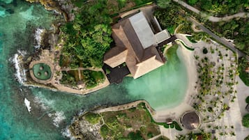 Vista aérea de un complejo turístico con piscina, zona de playa y un edificio grande con techo.