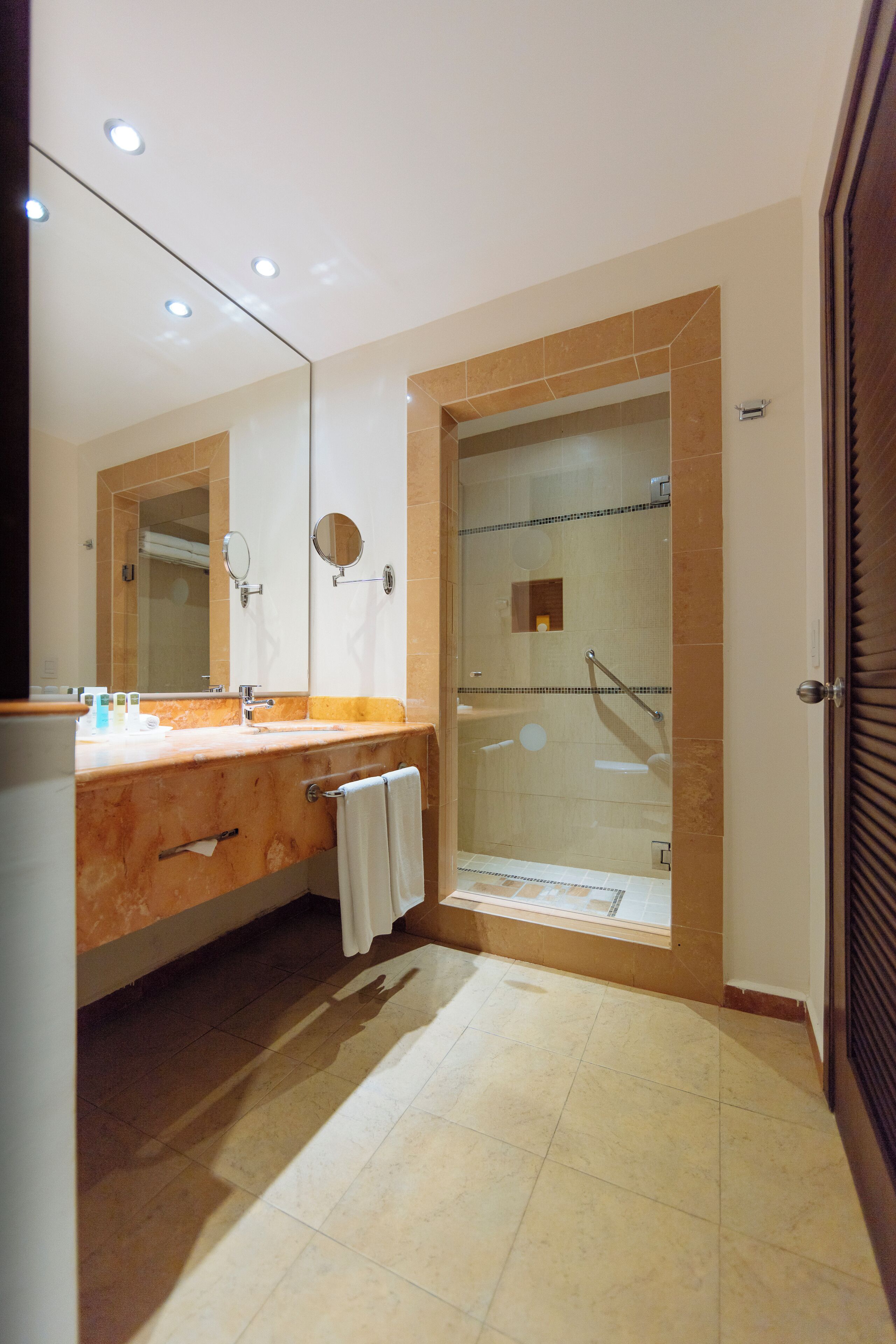 A modern bathroom with a marble vanity, a large mirror, a glass-enclosed shower, and a tiled floor.
