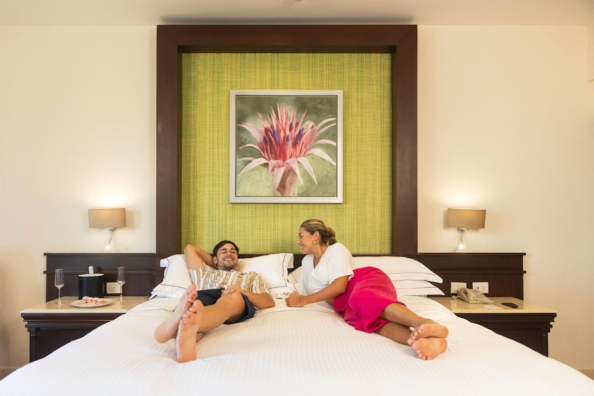 Ein Hotelzimmer mit einem großen Bett, zwei Nachttischen, einer Wandlampe und einem floralen Bild im Rahmen über dem Bett.