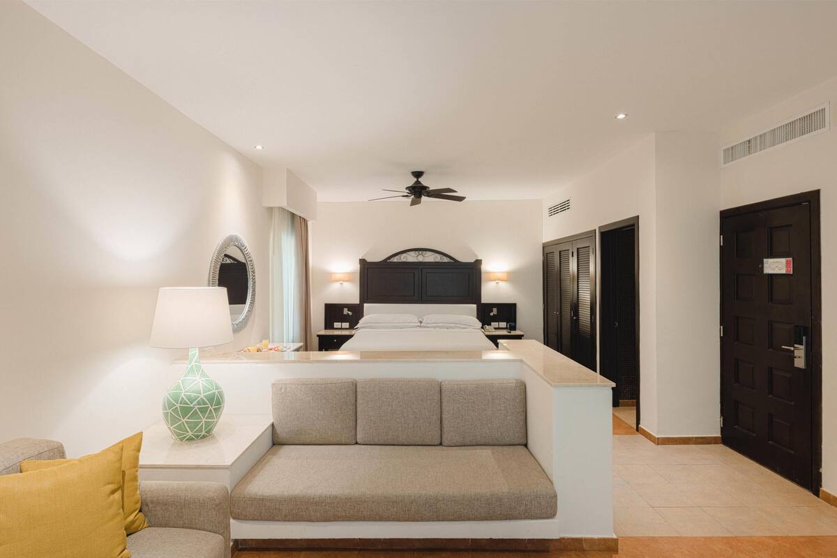 Ein modernes Hotelzimmer mit Bett, einer Sitzecke, einem Nachttisch mit Lampe und Deckenventilator.