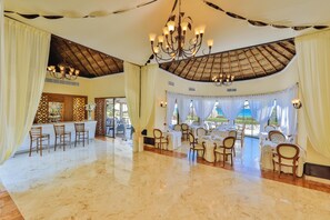 A spacious dining area with a high ceiling, chandeliers, and a view of the ocean.