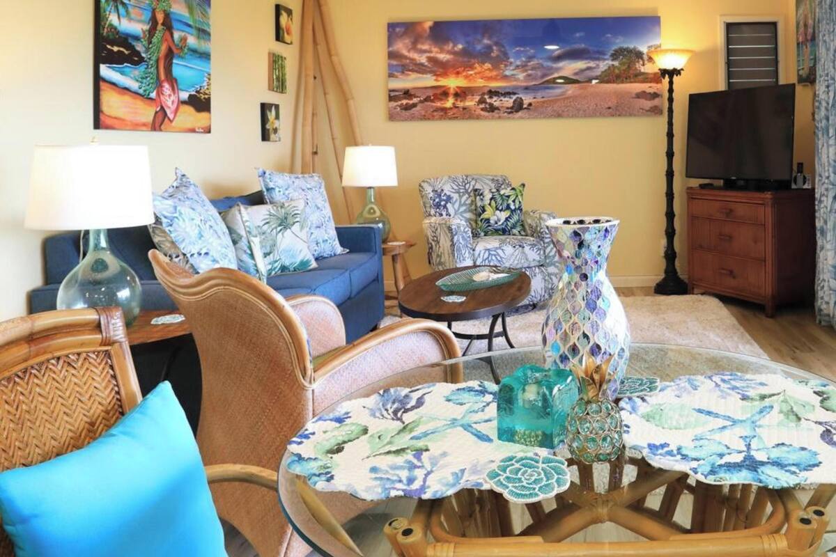 Un salon comprenant un canapé, des fauteuils, une table basse en verre et un téléviseur.