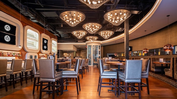 Un interior de restaurante moderno con suelos de madera, varias zonas de estar e iluminación decorativa.