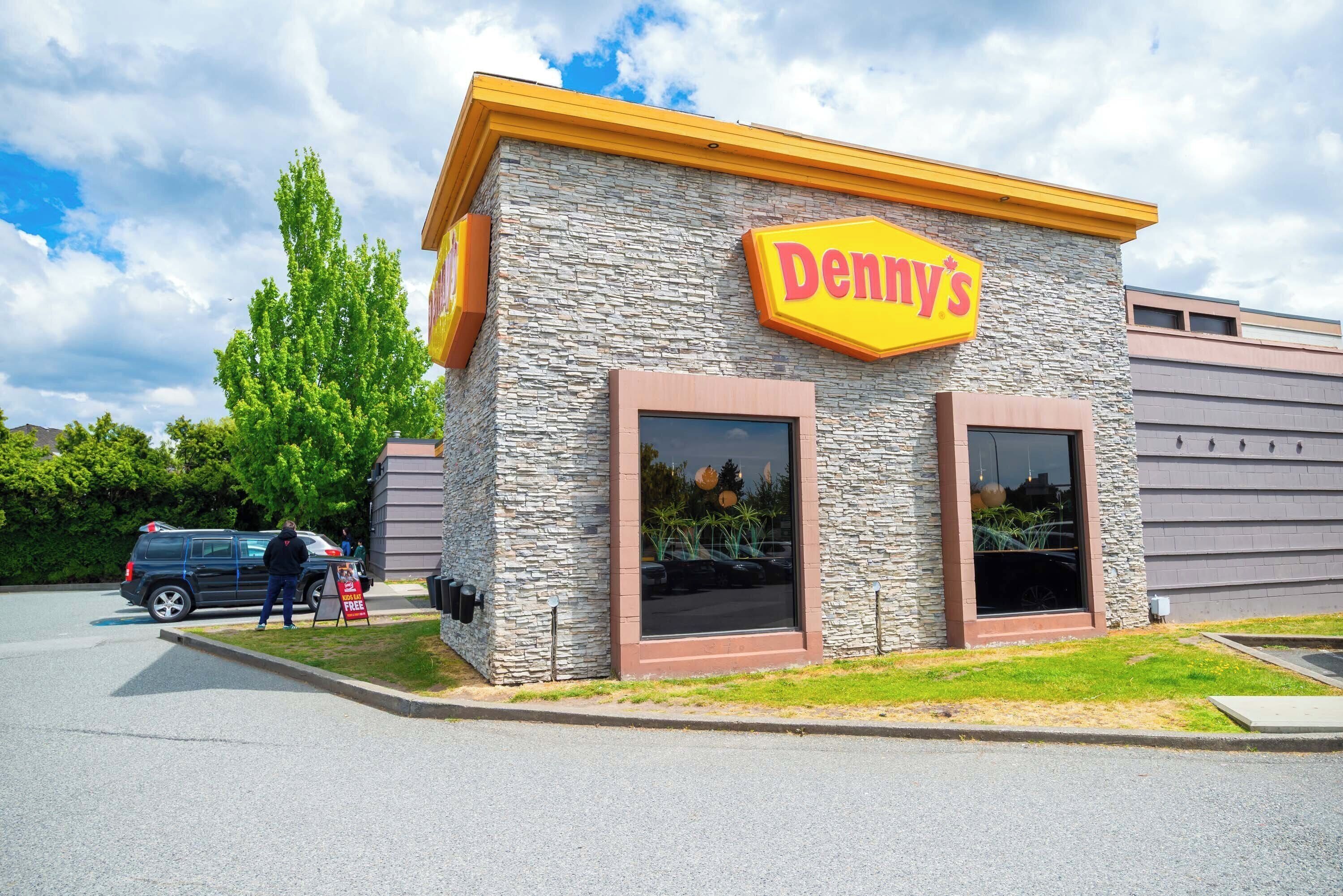 Un edificio con fachada de piedra y un gran letrero amarillo que dice "Denny's".