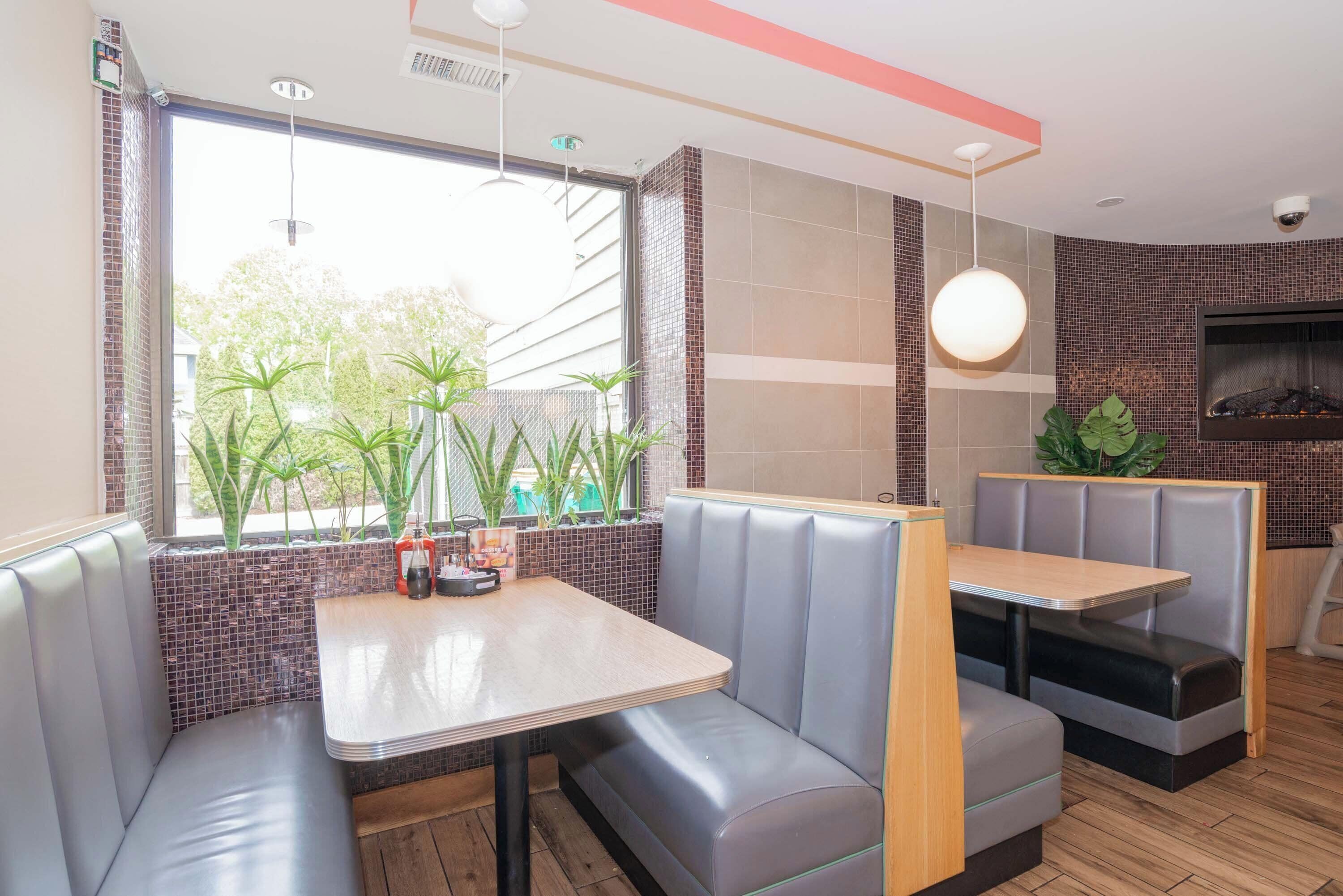 A restaurant interior with booth seating, a large window with plants, and a tiled backsplash.