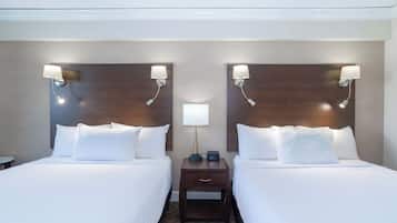 A hotel room with two beds, each with white linens and pillows, a nightstand with a lamp and a clock, and a wall-mounted light fixture.
