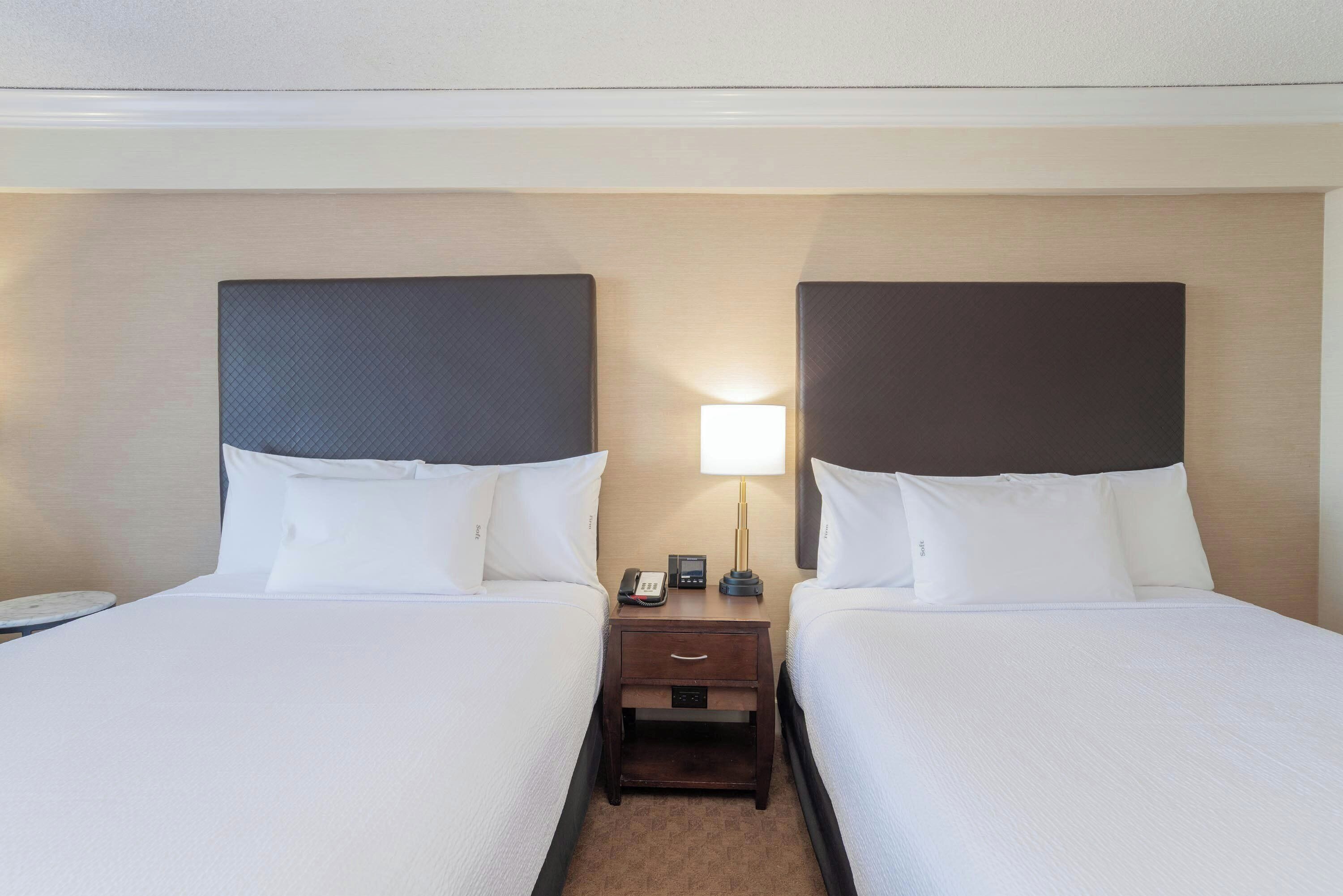 A hotel room with two beds, a nightstand with a lamp, and a phone.