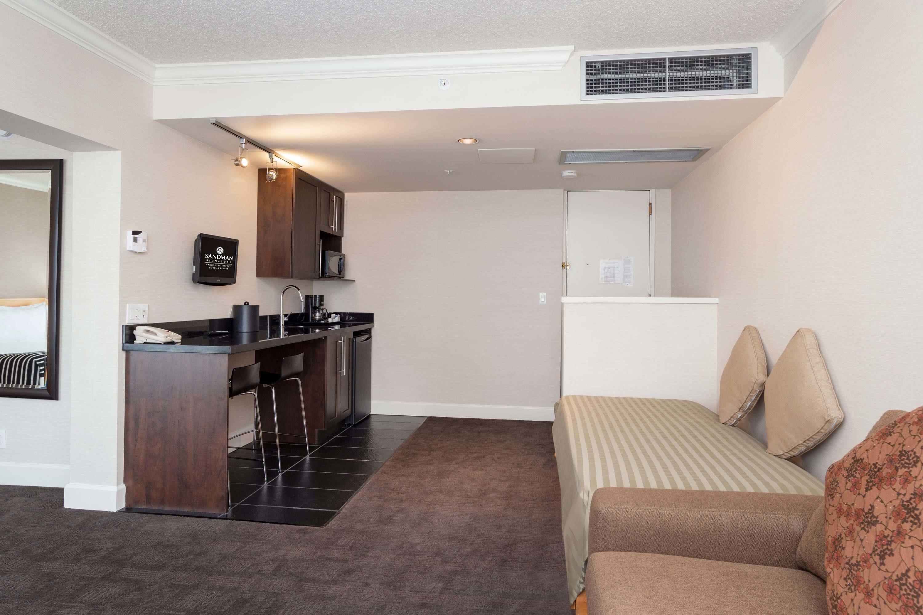 Una habitación de hotel compacta con kitchenette, una cama con ropa de cama a rayas y una pequeña zona de estar.