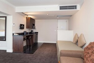 Una habitación de hotel compacta con kitchenette, una cama con ropa de cama a rayas y una pequeña zona de estar.