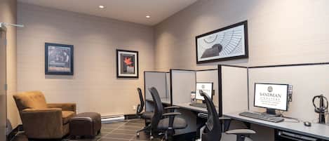 A modern office space with cubicles, a brown armchair, and a computer desk with a monitor, keyboard, and headphones.
