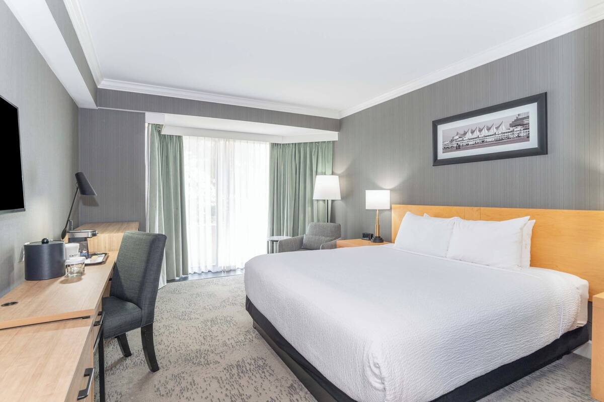 Une chambre d’hôtel avec un grand lit, un bureau avec une chaise, une télévision et une fenêtre avec des rideaux.
