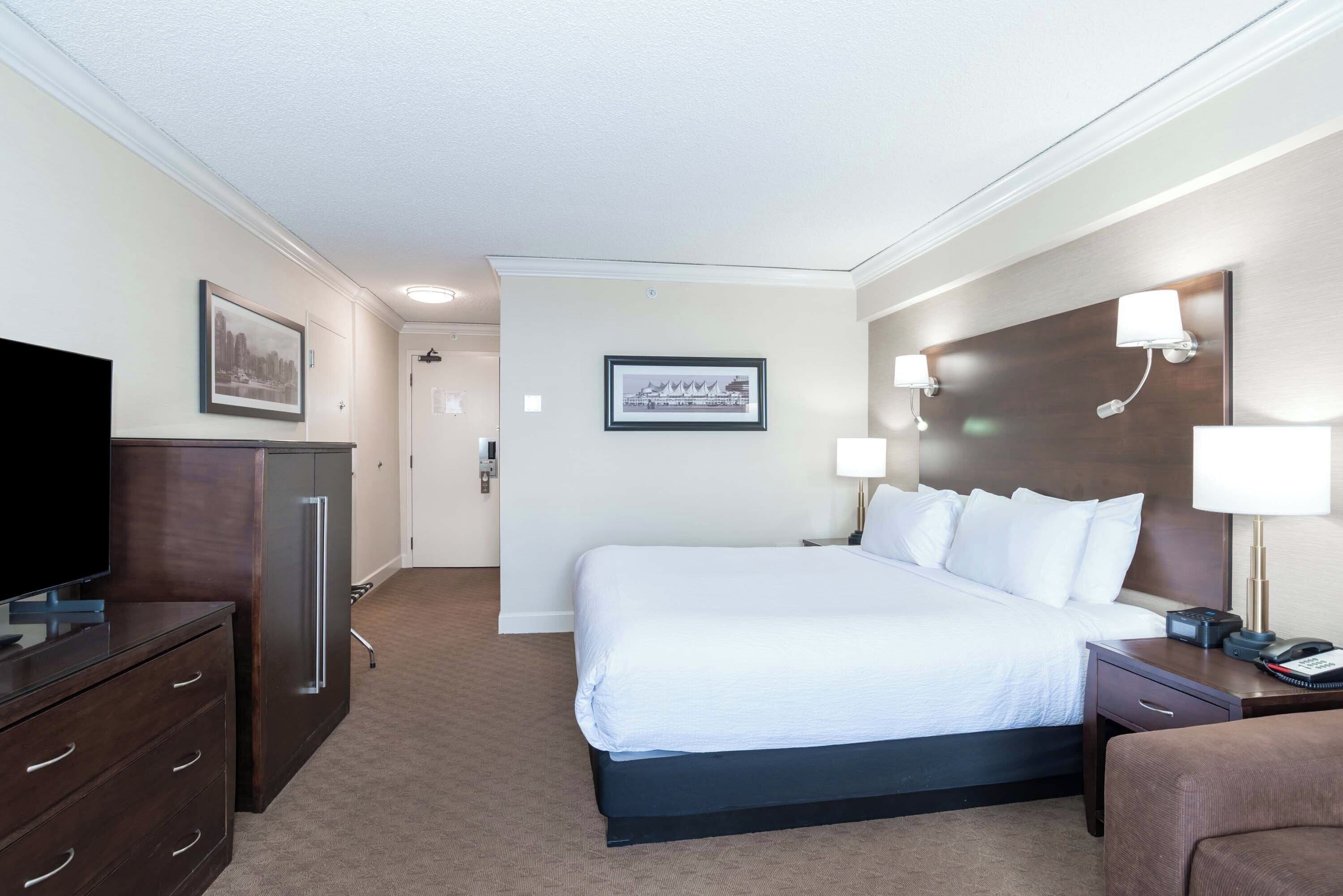 Una habitación de hotel con una cama grande, televisor, escritorio y cómoda.