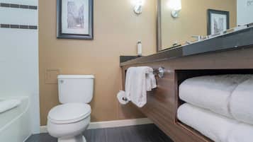 Un baño con inodoro, lavamanos con espejo, toallero con toallas y un cuadro en la pared.