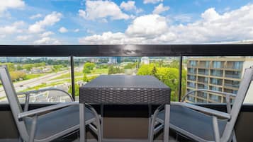 Een balkon met een tafel en twee stoelen, met uitzicht op een stadsgezicht met gebouwen en groen.