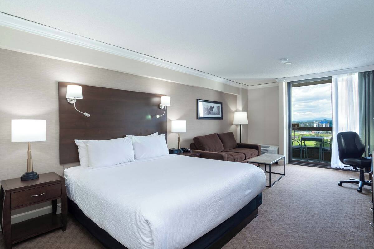 Une chambre d’hôtel avec un grand lit, un bureau, une chaise et une vue sur l’extérieur.