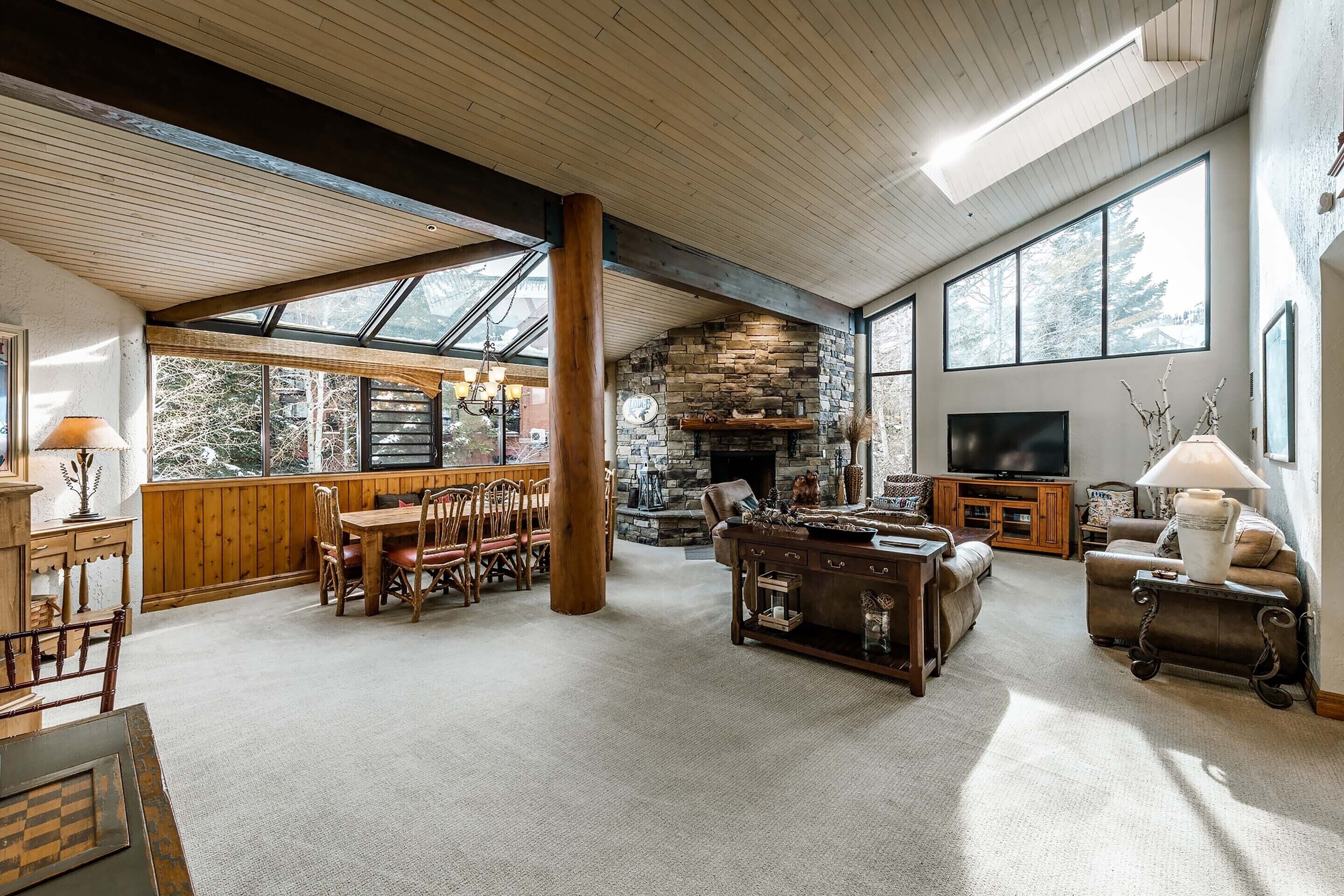 Un salón amplio con chimenea de piedra, muebles de madera y ventanas grandes.