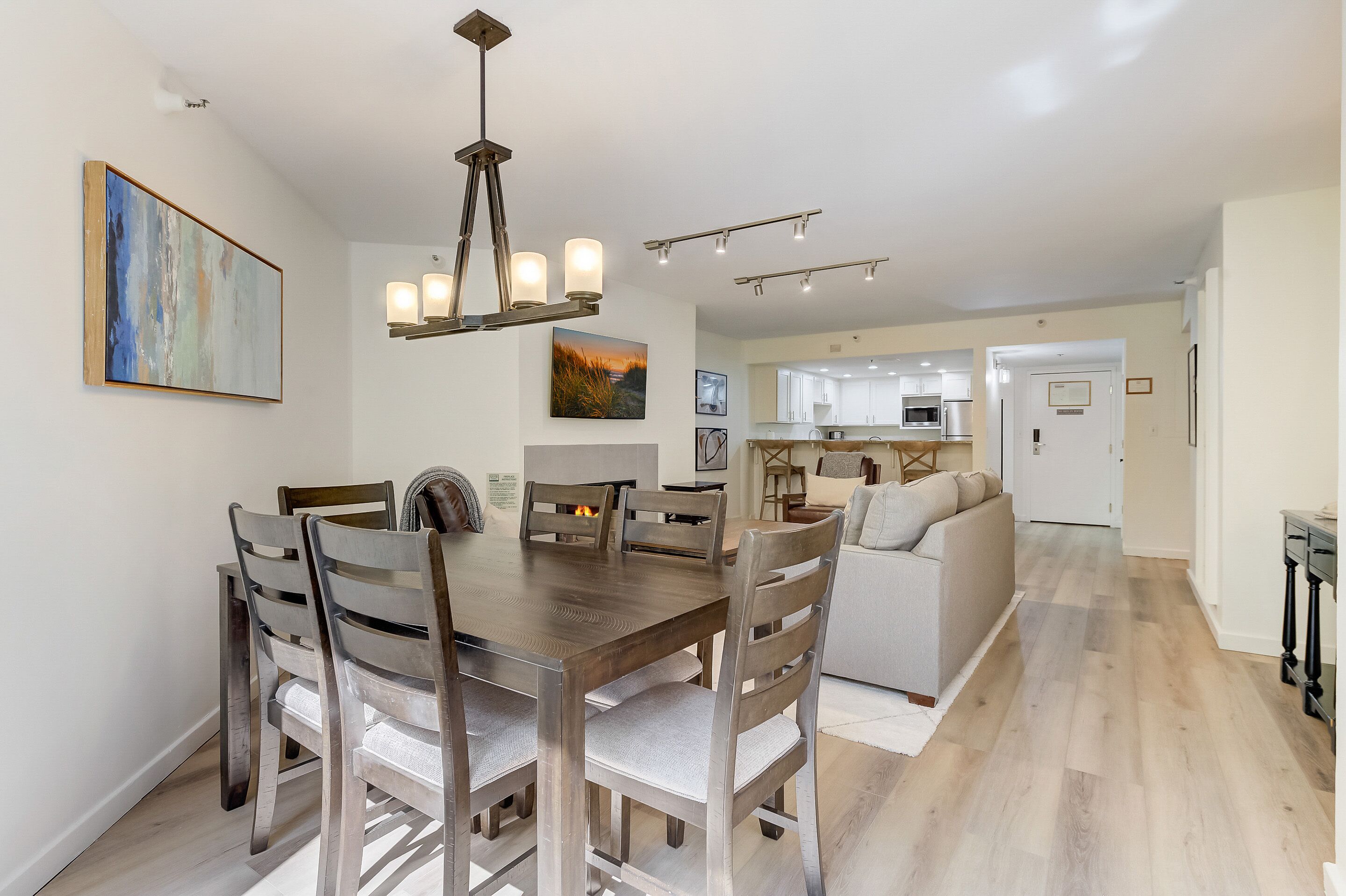 A spacious dining area with a wooden table and chairs, a chandelier, and a view into the kitchen.