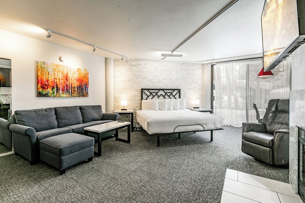 Una sala moderna con sofá, reposapiés, mesa de centro y cama con cabecera.