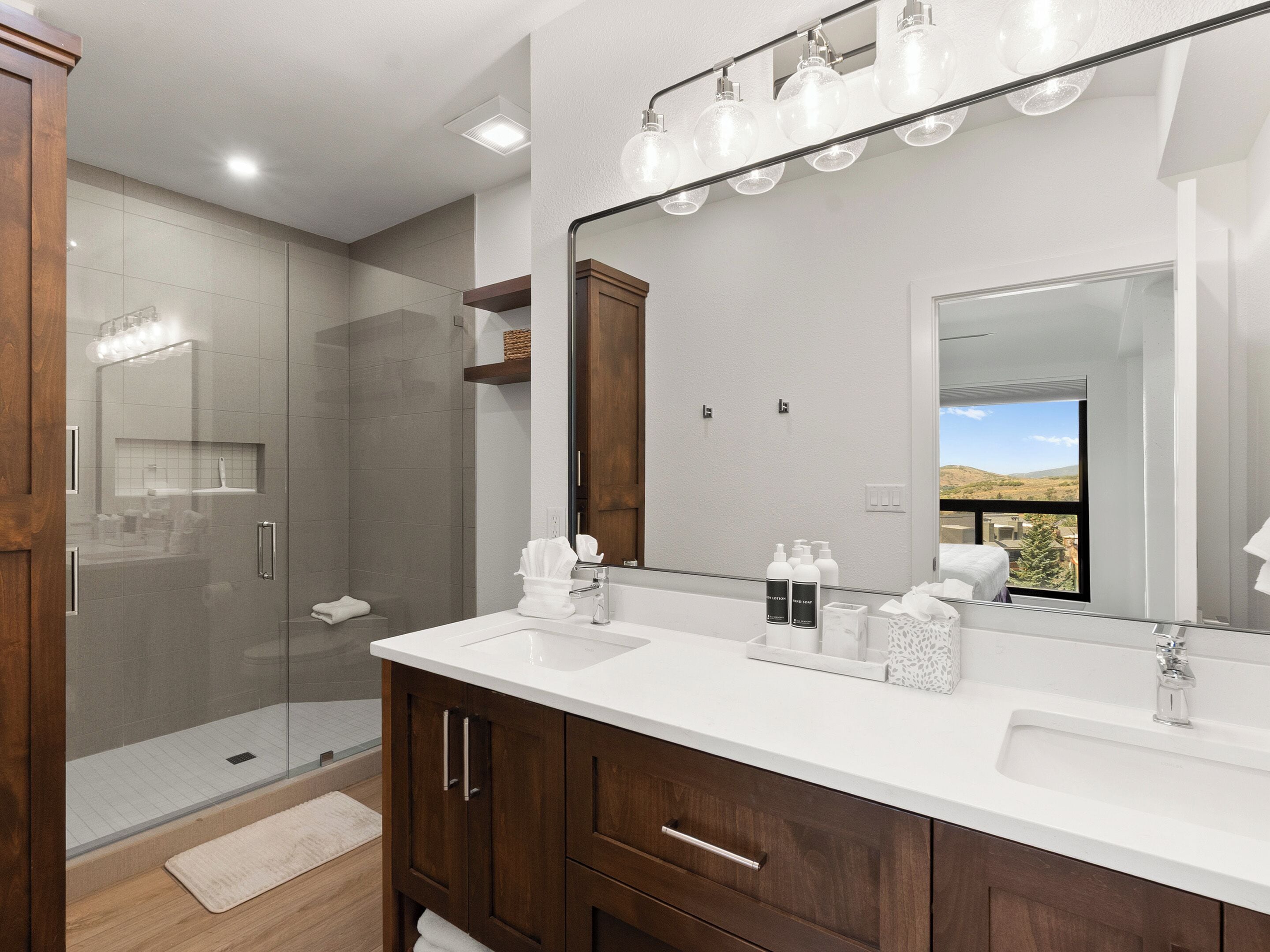 A modern bathroom with a glass shower enclosure, a large mirror, and a vanity with a white countertop.
