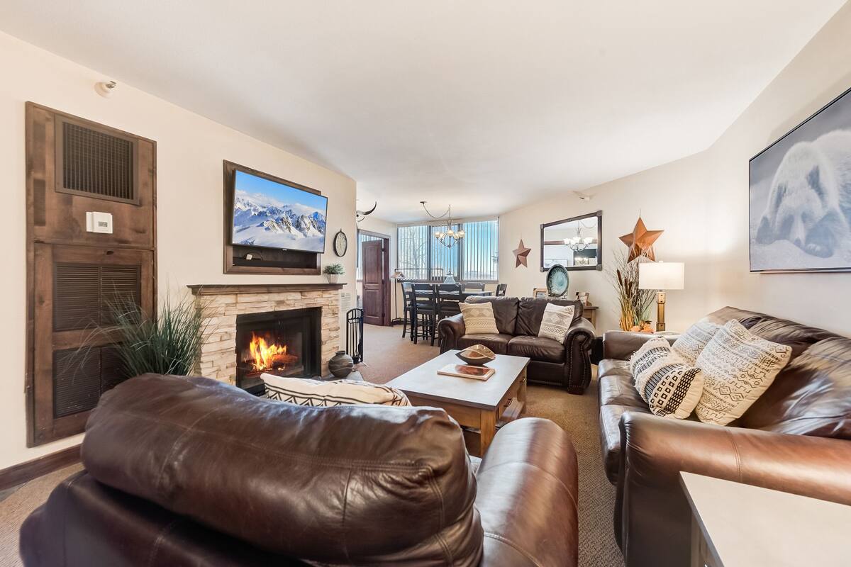 Una sala de estar acogedora con chimenea, sofás de cuero, un comedor y un televisor grande.