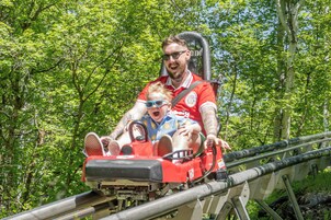 A person in a red shirt on a ride, surrounded by greenery.