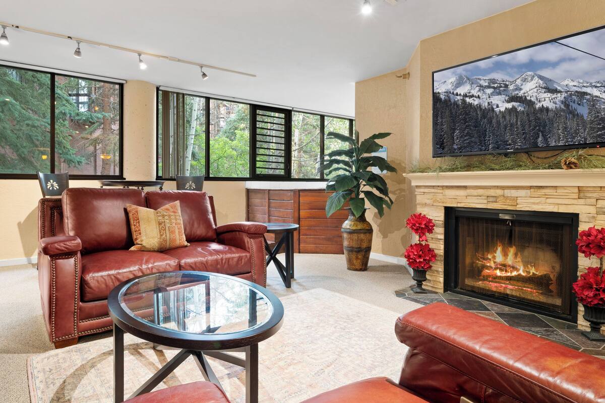 Una sala de estar moderna con sofás de cuero, una mesa de centro de vidrio, una chimenea y un televisor grande montado en la pared.