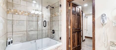 A bathroom with a glass-enclosed shower, a bathtub, and a wooden door.
