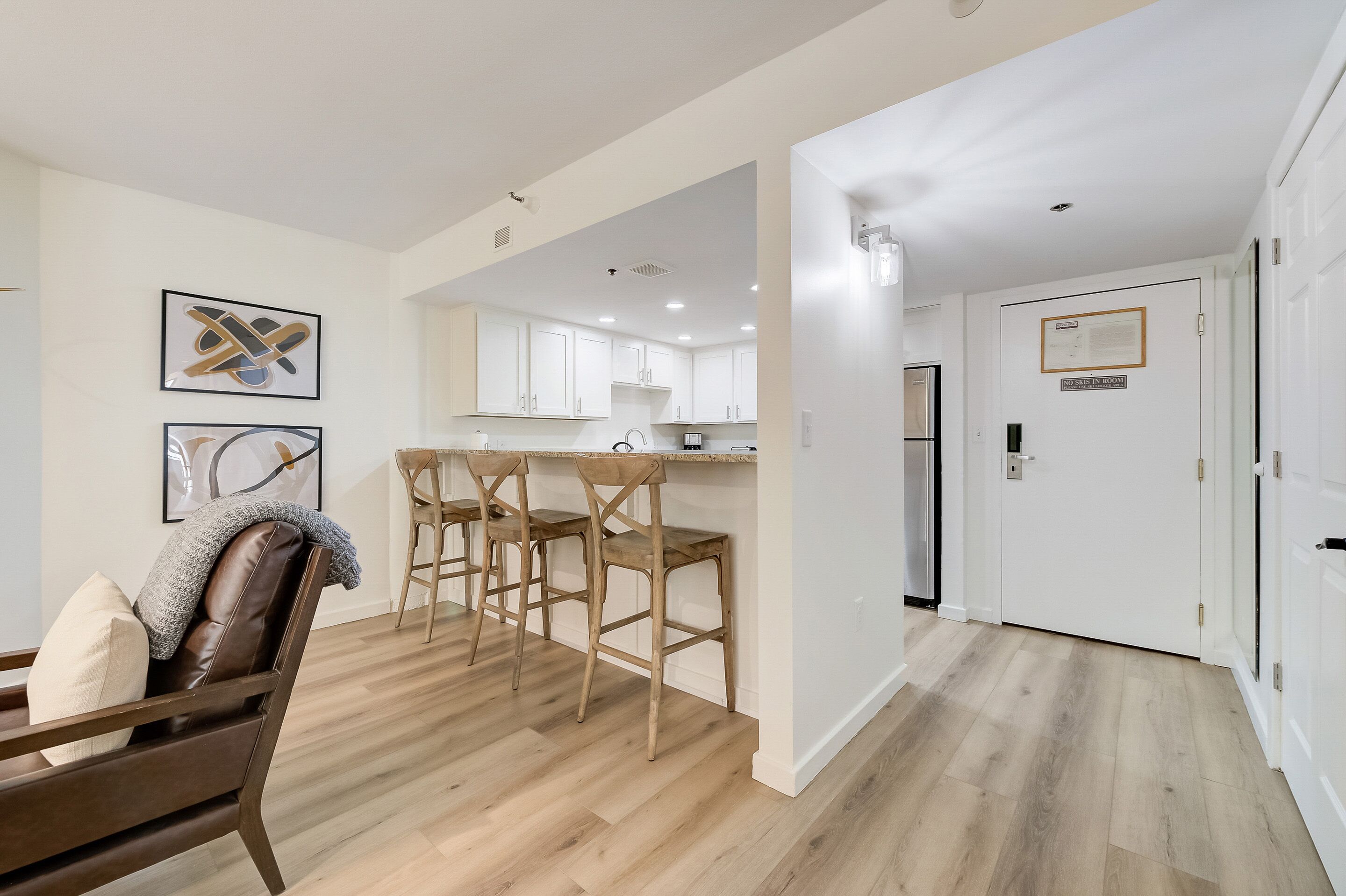 A modern kitchen with white cabinets and a central island, a dining area with wooden chairs, and a hallway leading to a door marked "No Sale in Room".